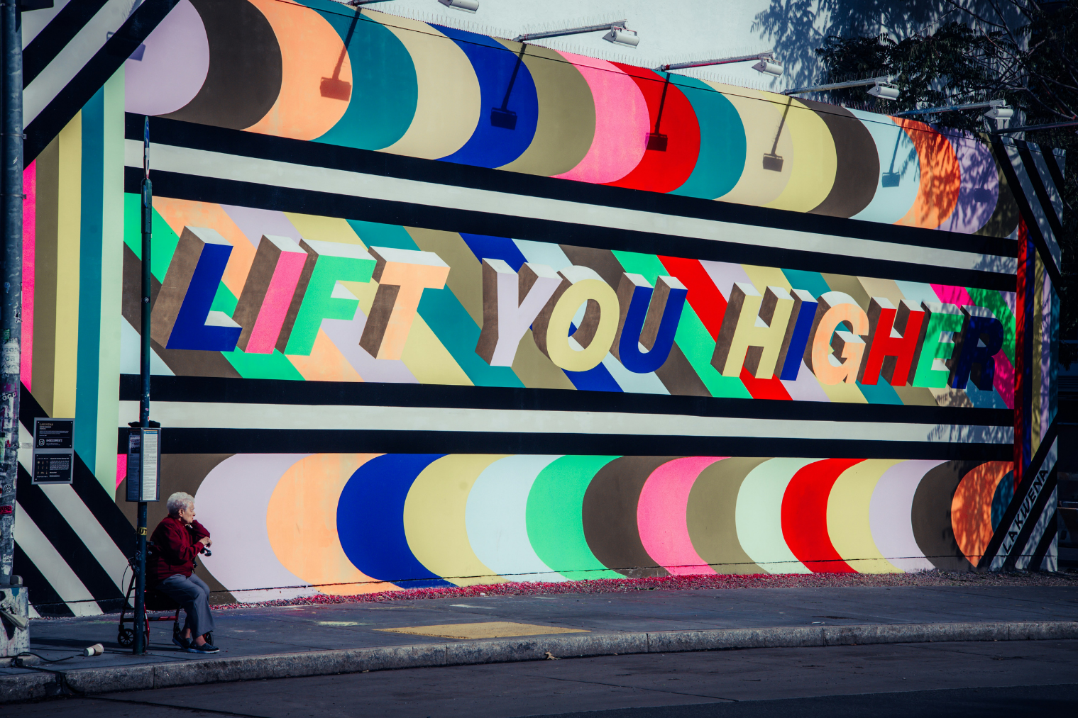 Kleurrijk geschilderde muur met de tekst, eveneens in kleurrijke drukletters: 'Lift you higher'.